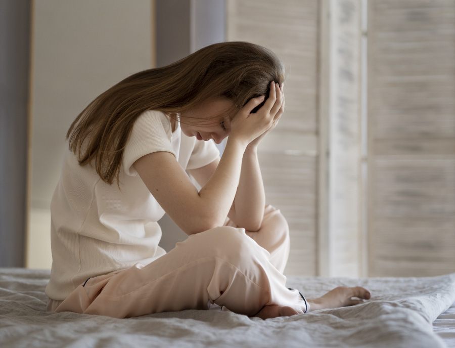 한 젊은 서양 여성이 불면증 때문에 침대에 앉아서 양쪽 손을 머리에 대고 고통스러워 하고 있는 것을 찍은 사진