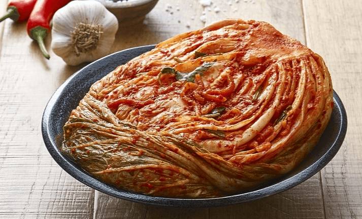 접시에 배추김치 반포기가 담겨있고, 그 뒤에 마늘 한통과 빨간 고추 2개가 있다.