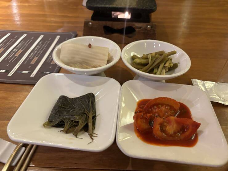 하얀 접시에 반찬 4가지가 담겨있다.
반찬은 백김치, 궁채장아찌, 와사비잎 장아찌, 토마토김치이다.