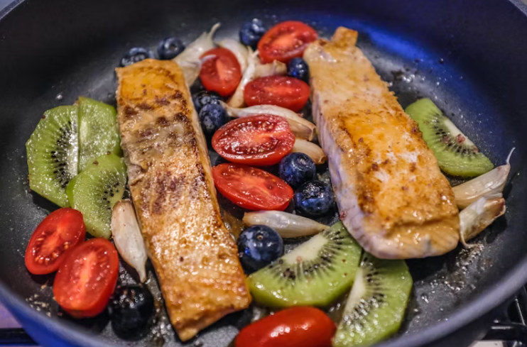 뇌 건강에 좋은 연어, 블루베리, 키위, 토마토, 마늘 등으로 구성된 식단이 팬에 구워지고 있는 모습