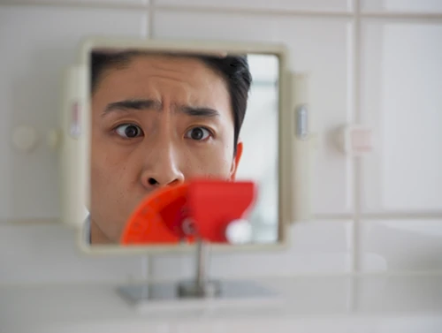 깨끗한 욕실 거울에 비친 사람의 놀란 눈 클로즈업. 거울 가장자리에 초점이 맞지 않는 붉은색 얼룩이 희미하게 보여 혈변 발견 시의 놀람과 걱정을 암시하는 장면.