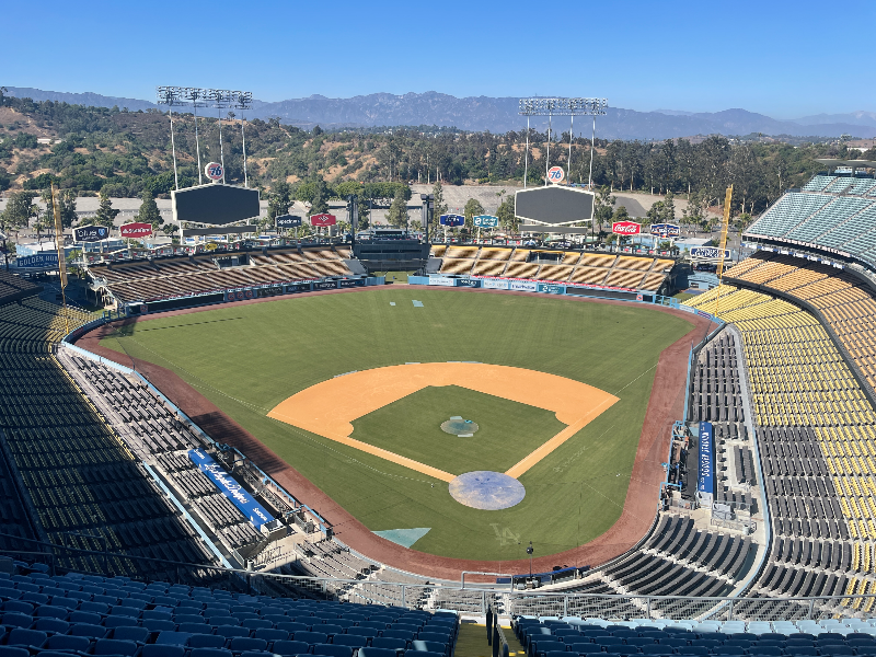 다저 스타디움의 전경이다. 매우 큰 경기장이 산으로 둘러싸여 있다. 언덕 안에 폭 들어가 있는 구조로 되어 있고 좌우 대칭의 모습이다. 홈 플레이트 쪽에서 바라본 모습으로, 앞쪽으로 양쪽에 큰 전광판 두 개와 여러 광고판들이 보인다.