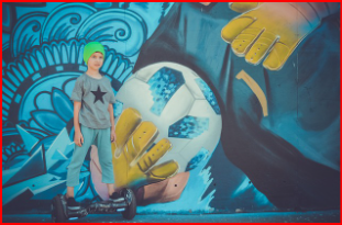 축구 벽화 앞에서 보드 위에 서 있는 청소년의 자유로운 모습