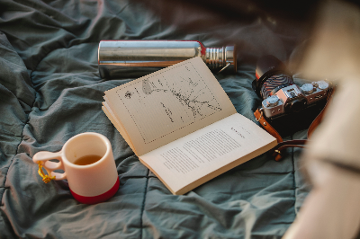 여행지에 돗자리를 깔고 텀블러, 책, 카메라, 컵을 올려둔 사진