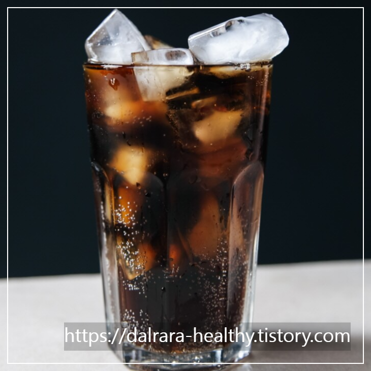 유리컵에 탄산음료와 사각 얼음이 담겨 있으며 컵 속에 기포가 보임
