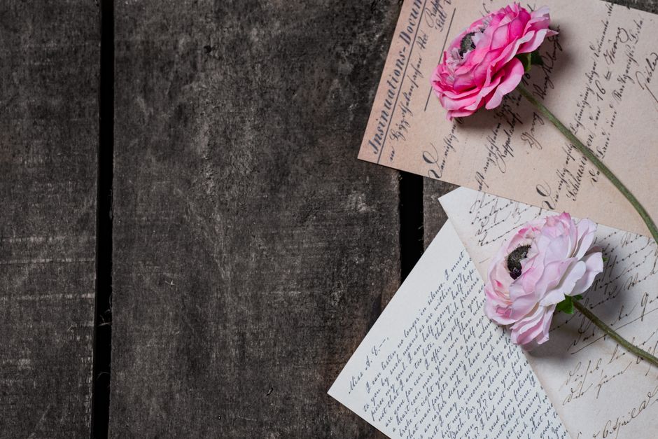 Delicate pink roses rest atop vintage handwritten letters on a rustic wooden table.