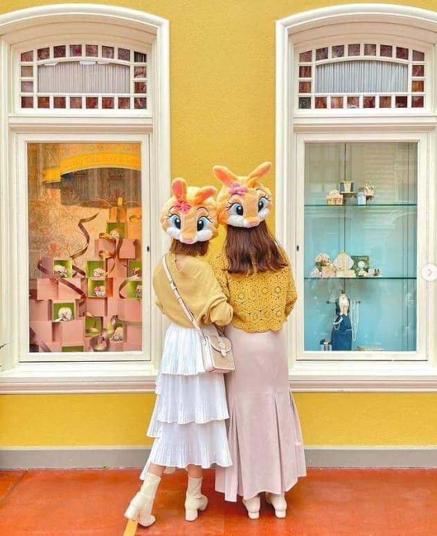 노란색 벽 앞에서 2명의 여성이 벽을 보고 서 있다.