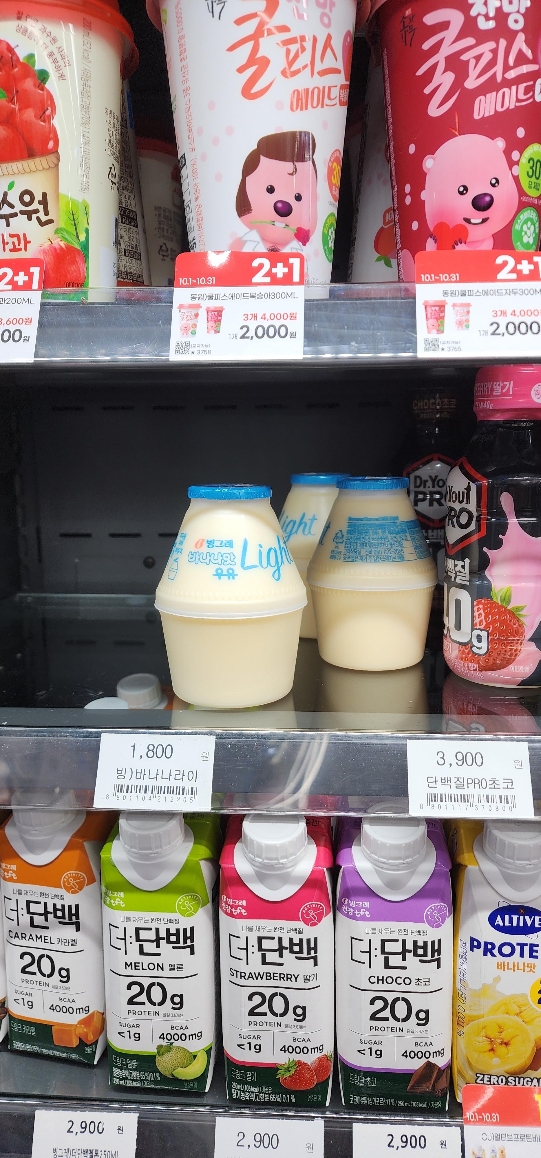 Convenience store refrigerator shelf displaying Binggrae Banana Milk Light bottles alongside Korean protein drinks and fruit-flavored beverages — popular Korean drinks showing local snack culture and trends.