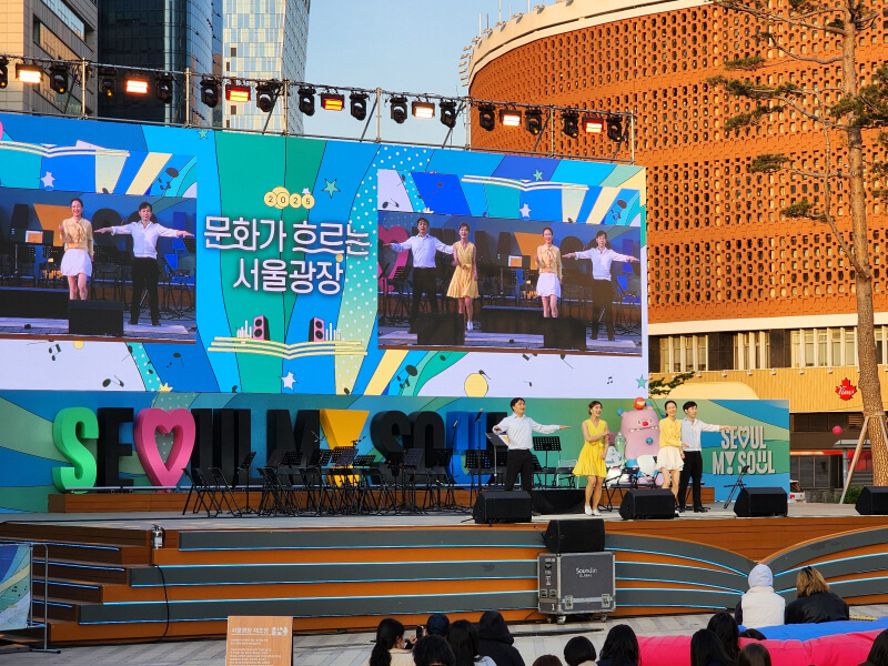 문화가 흐르는 서울광장 낮 공연 무대에서 뮤지컬 배우들이 단체 댄스를 선보이는 장면, 뒤편 대형 스크린에는 행사명이 표시됨