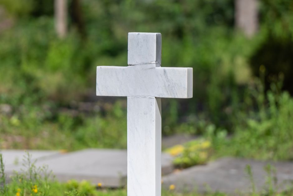 A serene marble cross in a lush green cemetery, symbolizing peace and remembrance.