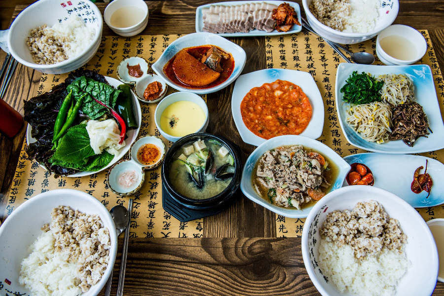 식당에서 파는 보리밥정식으로 테이블 위에 각종 쌈과 나물, 돼지고기 수육, 된장, 전, 불고기, 된장찌개, 보리밥 등을 4인분 놓아두고 찍은 사진