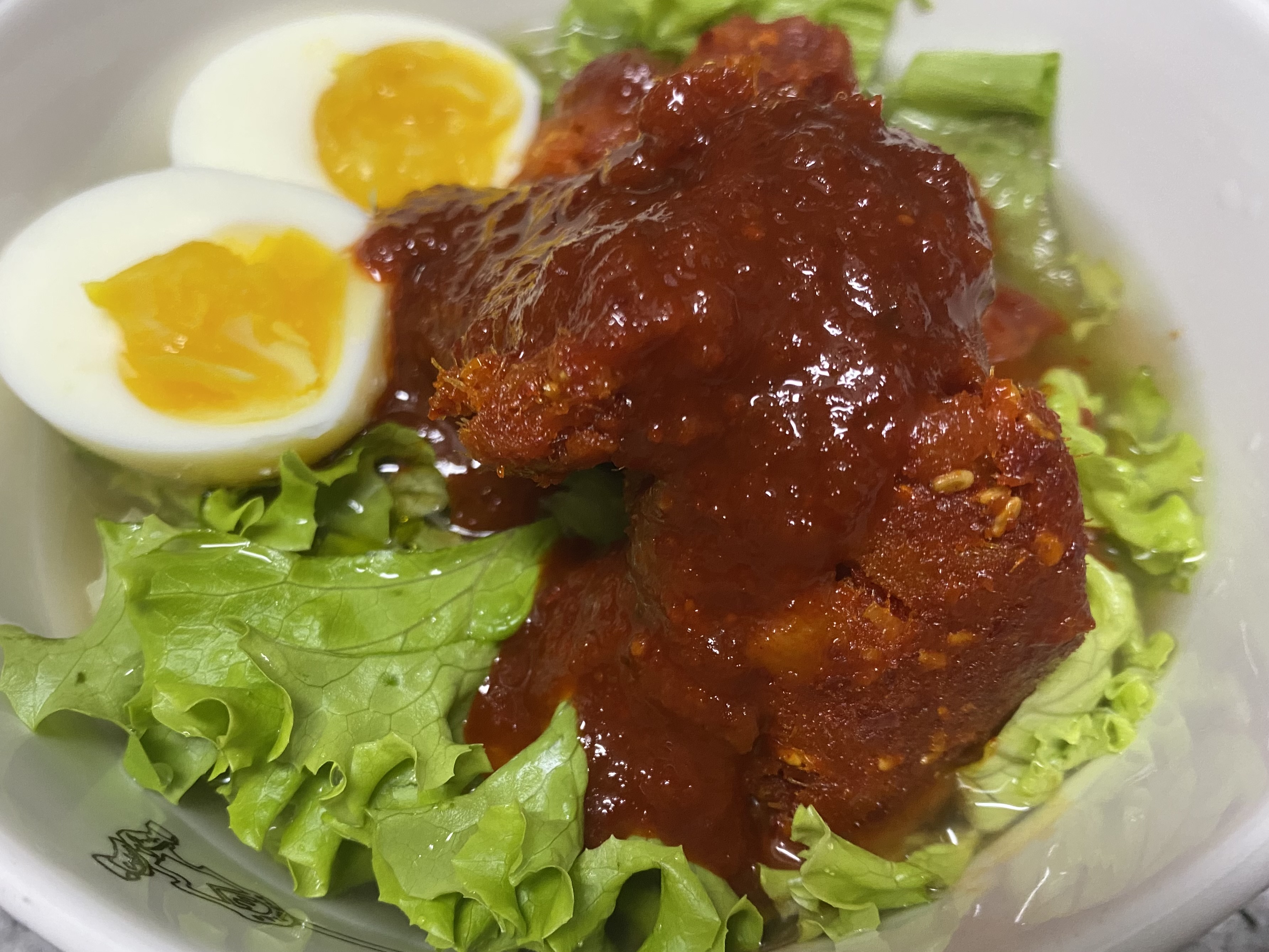 하얀색 도기그릇에 반숙란, 명태회절임, 양념장, 상추가 올려져 있는 냉면 사진입니다.