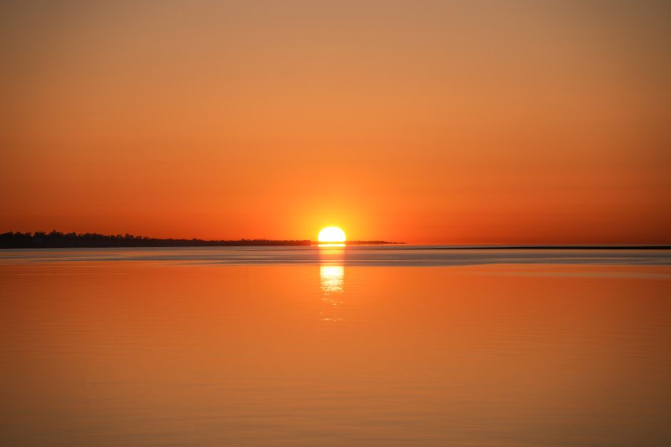A tranquil sunrise over a calm ocean, casting a warm golden reflection on the water.