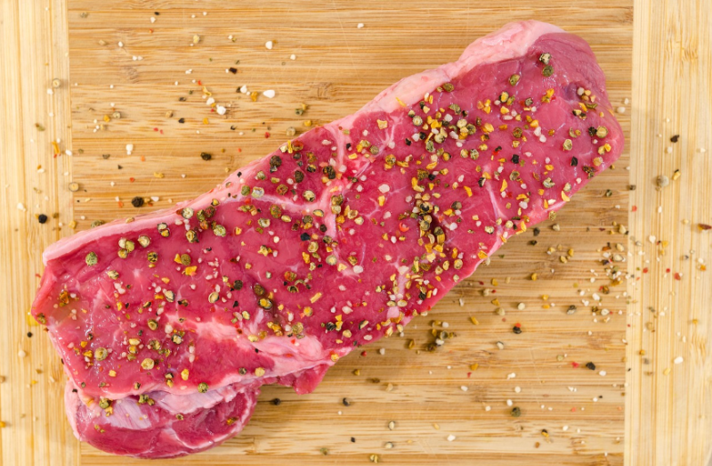 철분이 풍부한 붉은 소고기 위에 다양한 향신료가 뿌려진 이미지, 임산부의 철분 섭취와 영양 관리의 중요성을 나타냄