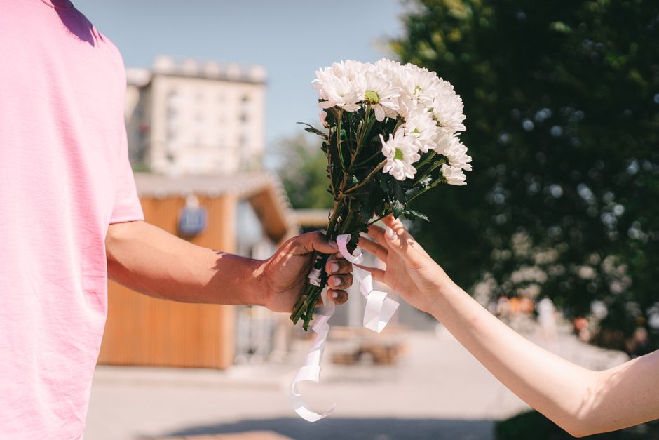 Close-up of couple exchanging a bouquet of white flowers on a sunny day.