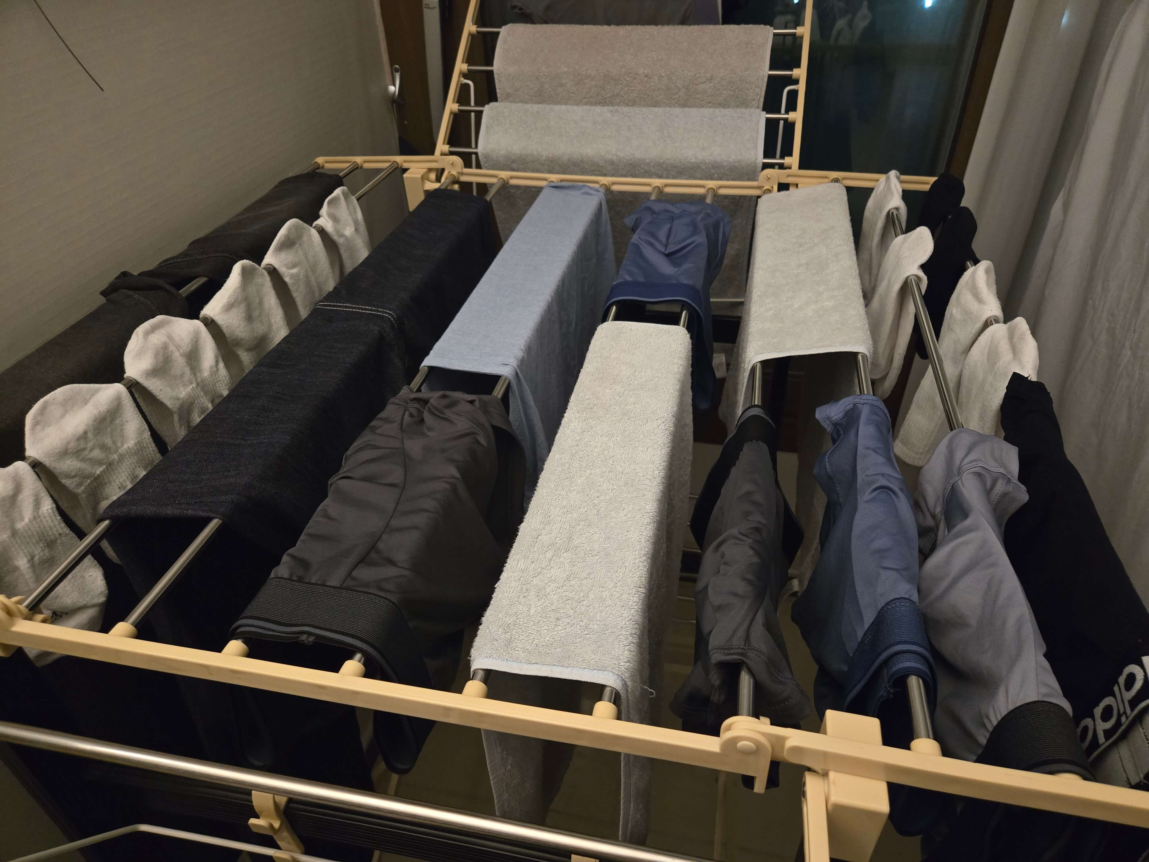 빨래 건조대에 많은 빨래가 널려 있고, 옆에는 이불까지 널려있는 사진