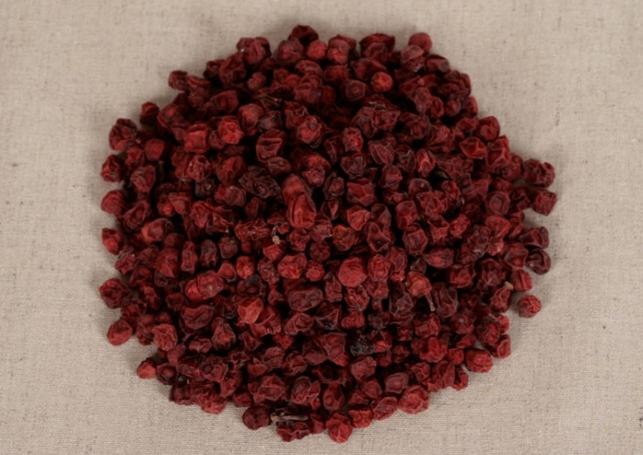 야생에서 채취를 한 붉은 색의 오미자를 잘 세척한 후에 건조시킨 것을 베이지색 바닥 위에 한움큼 놓아 둔 후에 위에서 찍은 사진