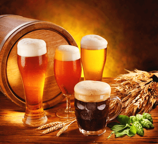 3개의 투명한 유리잔에 하얀 거품이 가득한 맥주가 가득하고, 1개의 잔에는 검정색 흑맥주가 있다. 뒤에는 나무로 된 맥주 드럼통이 있다.