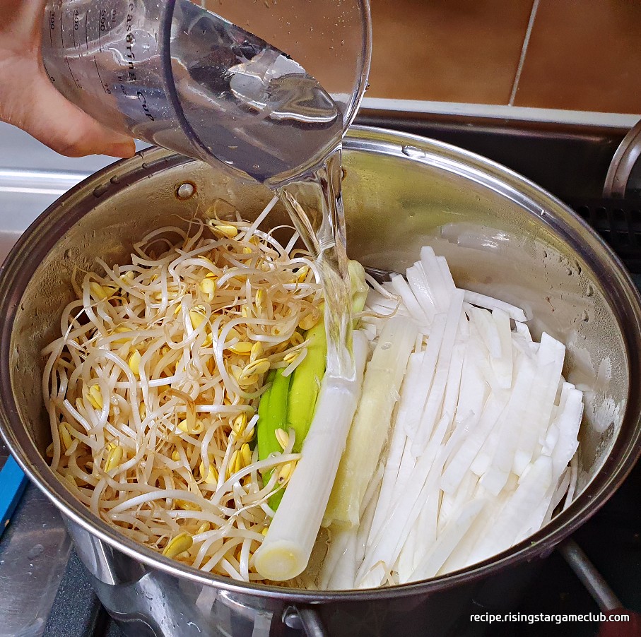 명절 나물국을 끓이기 위해 냄비에 콩나물과 대파, 무를 넣고 물을 붓고 있는 사진