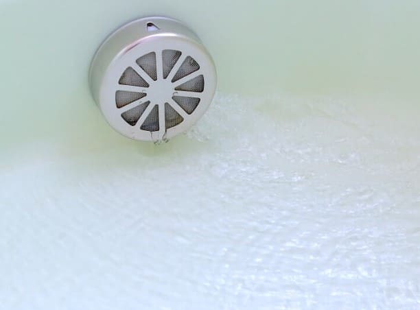 흰색 욕조 안에 작은 동그란 쇠 모양의 배수구가 있다