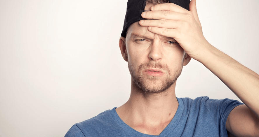 모자 쓴 남성이 이마에 손을 얹고 고통스러워 하고 있다