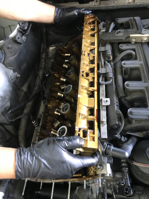 BMW 직렬 6기통 엔진에서 정비사가 실린더 헤드 커버와 캠샤프트를 탈거하고 있는 작업 장면