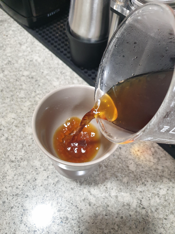 아이랜드 테이블 위에 놓인 그레이 컵에 커피 추출액을 따르는 모습.