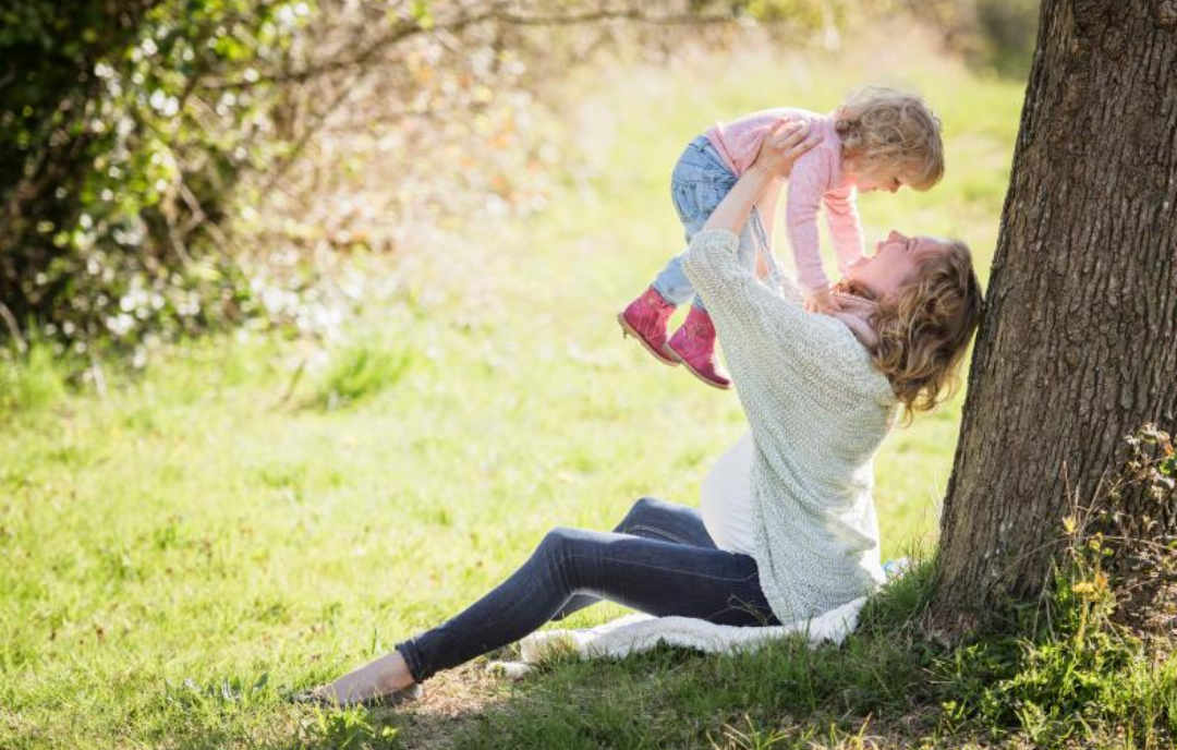 잔디밭에 엄마가 앉아 아기를 들어올리고 있다.