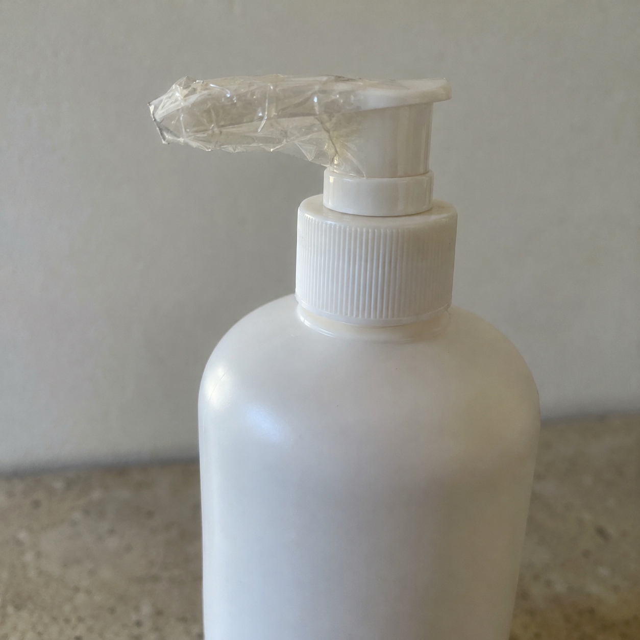 packing skincare for flight, close-up of a pump bottle with tape wrapped around its nozzle, plain background, no labels