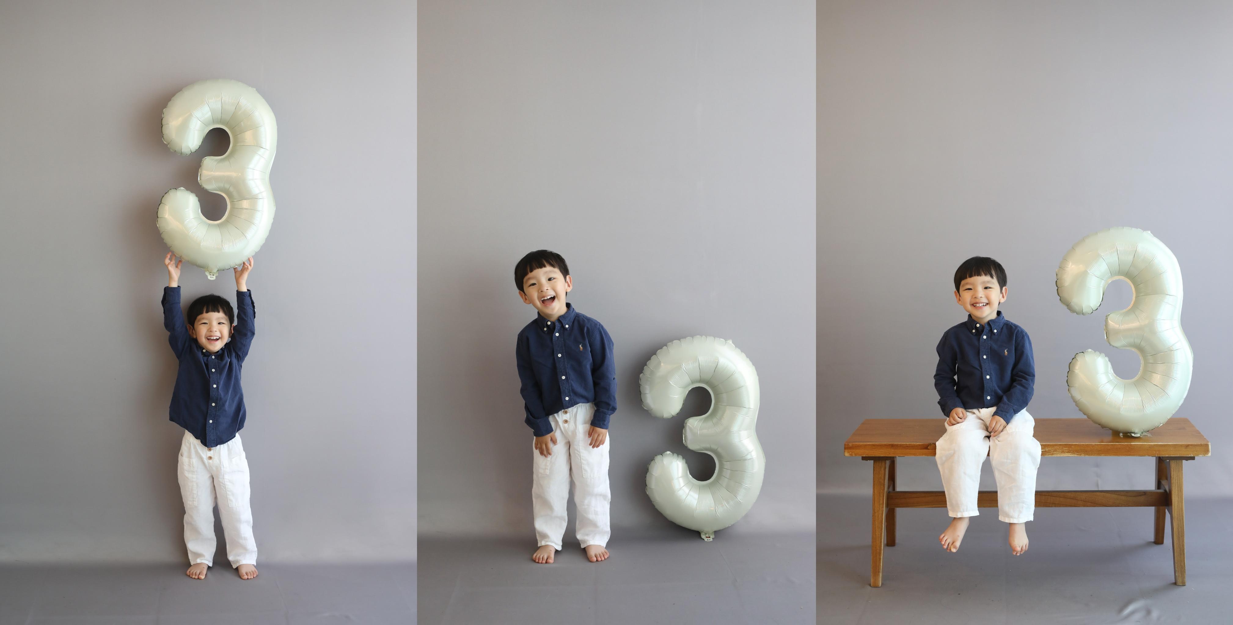 3돌을 맞은 아이가 흑백 배경 앞에서 숫자 3 풍선을 들고 다양한 포즈를 취하는 기념 사진. 감성적인 분위기 속에서 밝게 웃는 아이의 모습이 인상적이다.