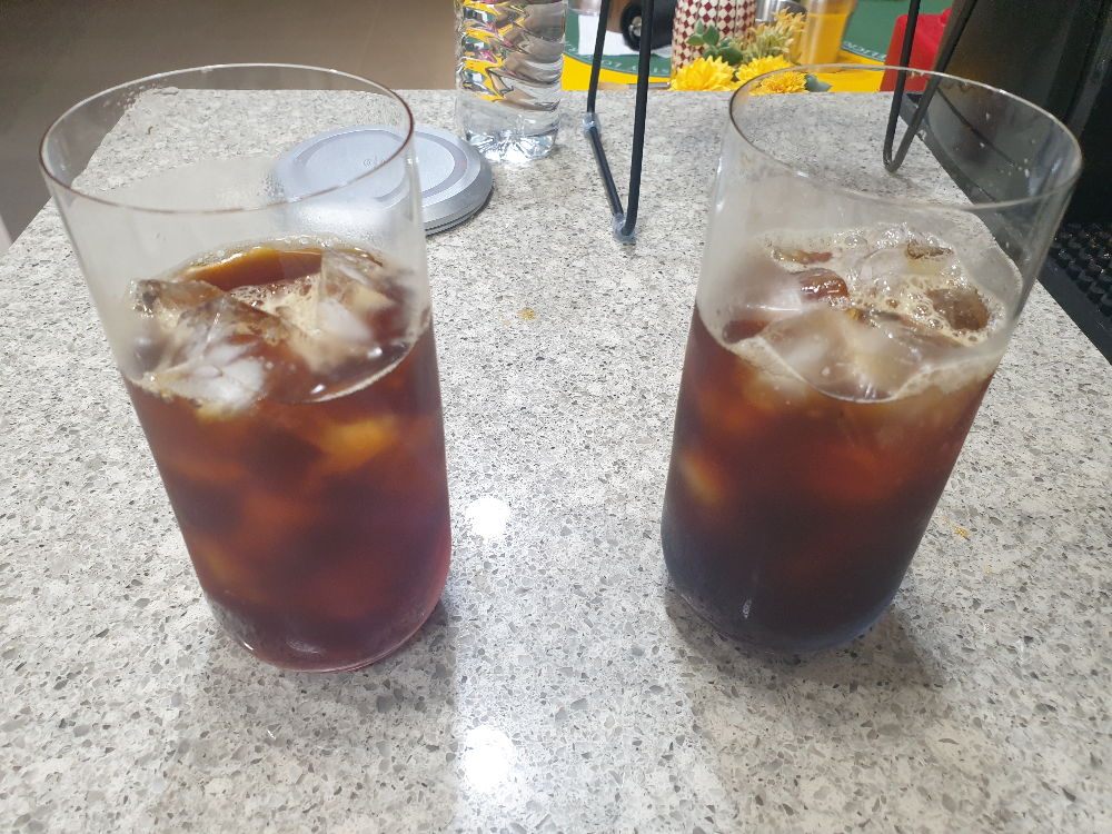 대리석 조리대 위에 두 잔의 아이스커피가 올려져 있다. 왼쪽은 반투명 붉은 컵, 오른쪽은 반투명 푸른컵