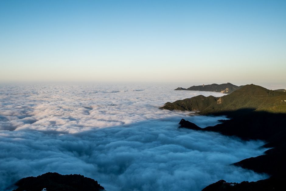 A breathtaking aerial view of mountain peaks rising through a sea of clouds at sunset.