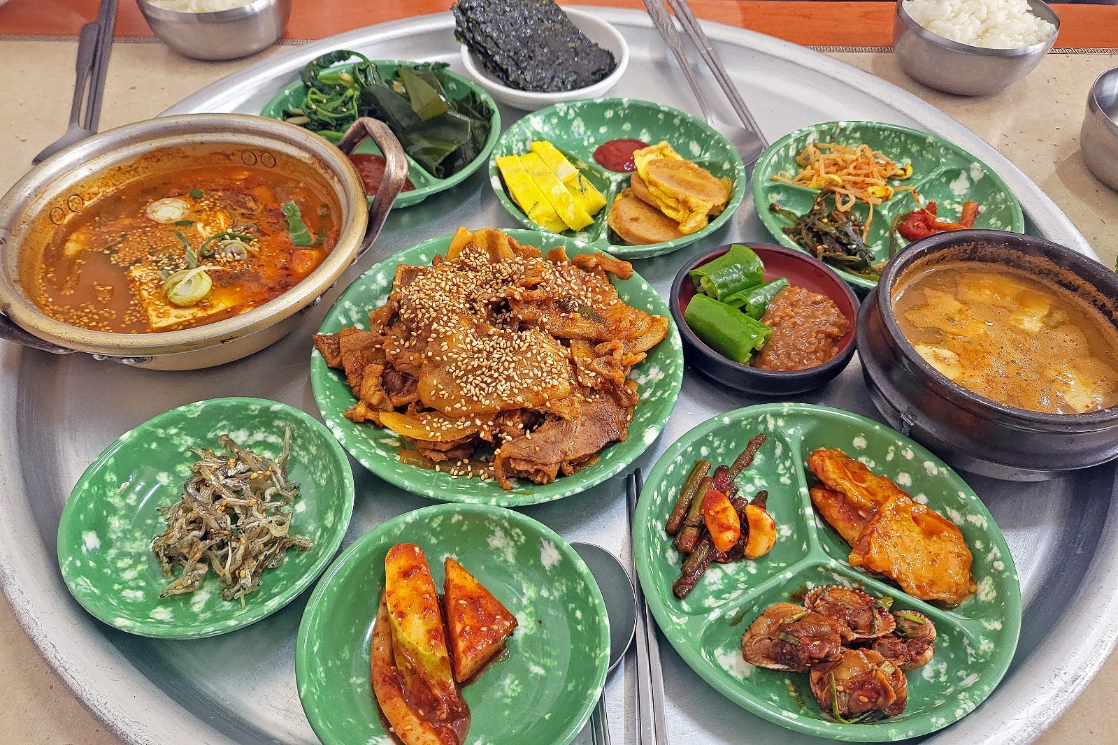 월성분식에서 김치찌개, 된장찌개, 제육볶음과 각종 반찬이 양은 쟁반에 담긴 모습