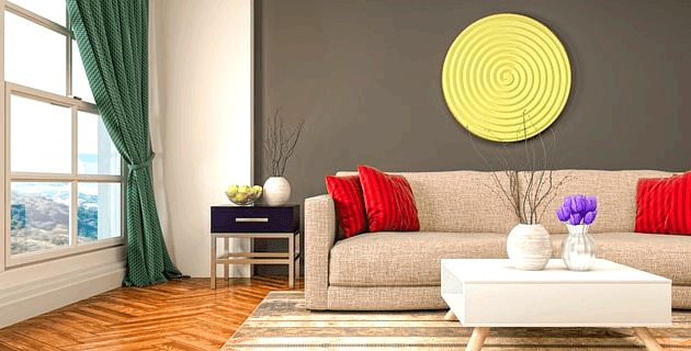 베이지색 소파가 있고 빨간 쿠션들이 여러개 올려졌다. 녹색 커튼이 창문에 있고 벽엔 둥그런 노란색 장식이 걸려있다.