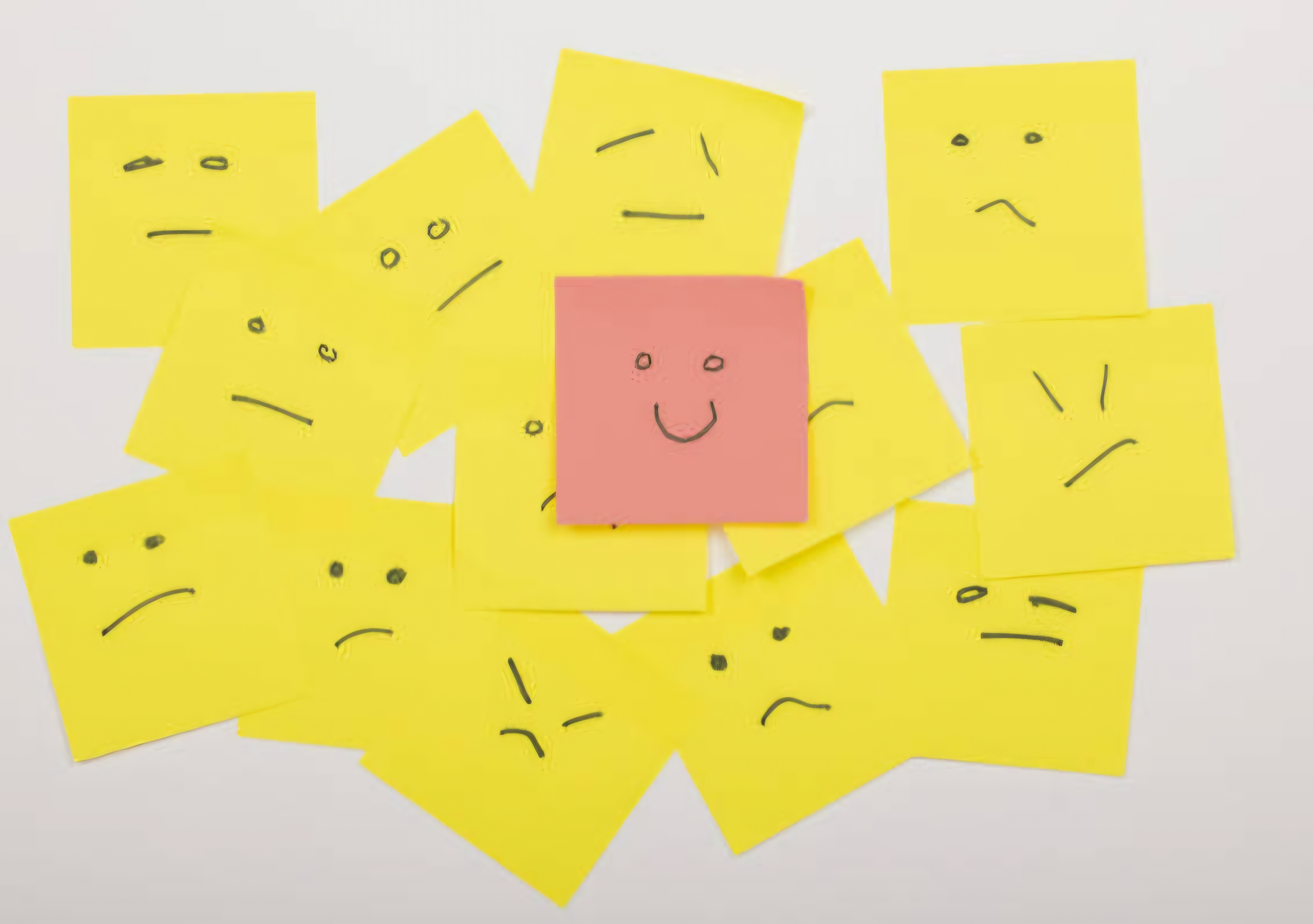 울상 짓는 표정이 그려진 포스트잇들이 있고 그 위에 웃는 표정이 그려진 포스트잇이 있음