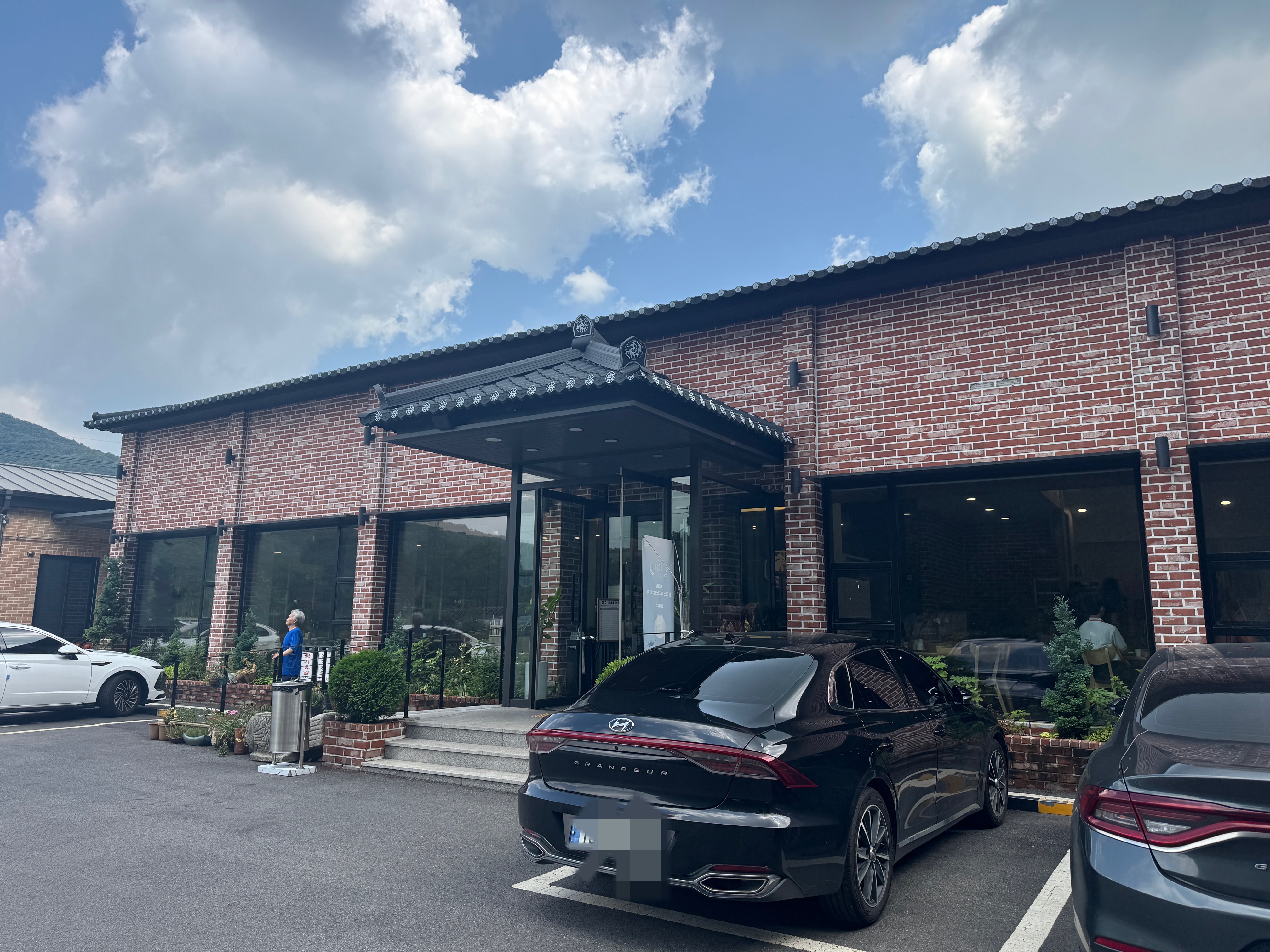 양지 아시아나CC 근처에 위치한 송정 닭갈비 외관. 붉은 벽돌 건물과 한옥 스타일의 지붕이 특징이며&amp;#44; 앞마당에는 주차된 차량이 보인다. 