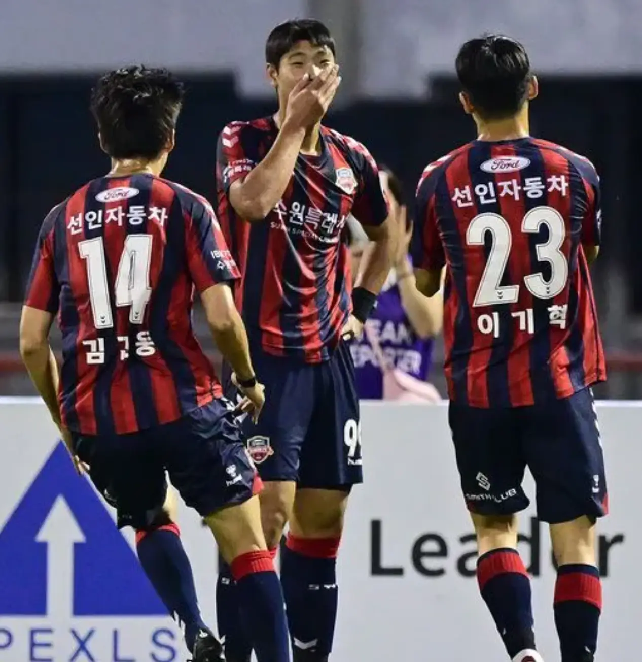 이영준- 붉고 파란 세로줄무늬 유니폼을 입은 이영준이 놀라 오른손으로 입을막으며 기뻐하고 동료 2명이 다가오는 뒷모습