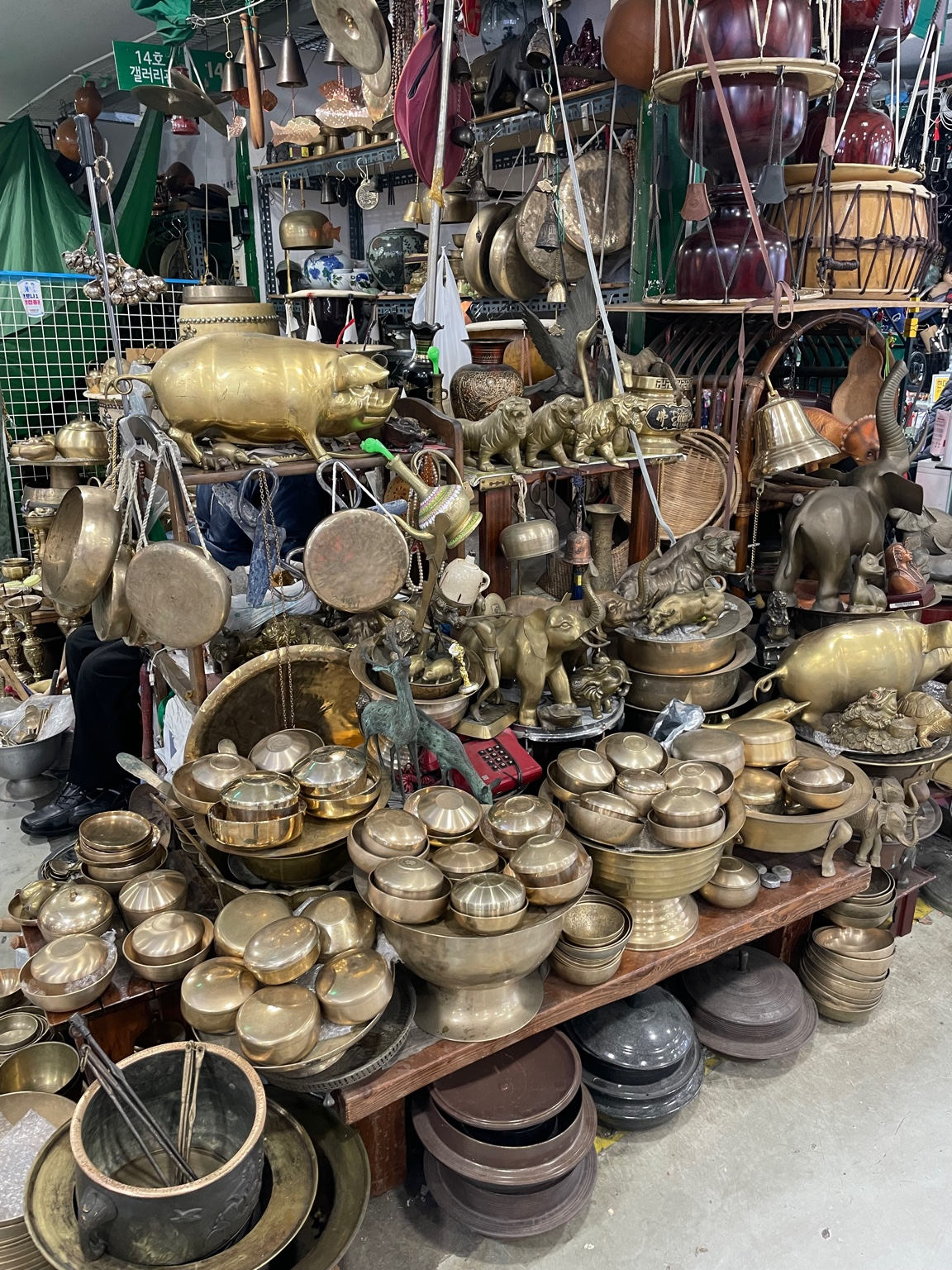 "A traditional metalware shop inside Seoul Folk Flea Market, filled with brass bowls, decorative gongs, and old Korean antiques."