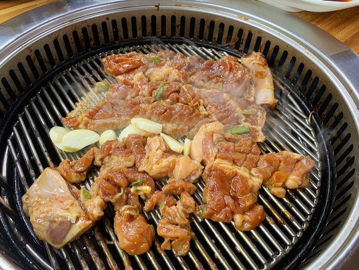 돼지갈비가 불판 위에 올려져 있고 고기 사이에 마늘과 파가 보인다.