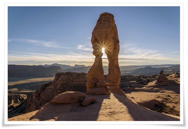 사막의 아름다운 풍경. 멀리 보이는 낮은 산들과 태양의 빛이 반사되는 아치모양의 바위가 인상적이고, 독특한 지형은 자연의 신비한 모습을 담고 있다