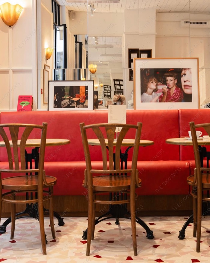 Cozy interior of Le Cafe en Rouje featuring a red leather banquette, wooden cafe chairs, and mirrors on the wall
