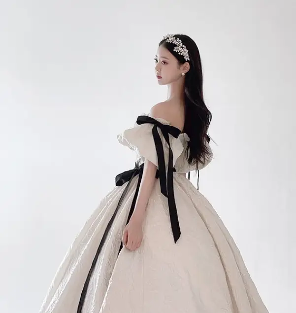 솔로지옥 3 - 베이지색 허리부분 아래가 넓고 긴 어깨가 드러난 드레스에 허리부분 검정색 리본끈과 팔부분 검정색 리분끈이 달린 드레스를 입고 머리를 길게 늘어뜨린채 머리에는 은색 꽃무늬 머리띠를 하고 옆으로 서있는 유시은