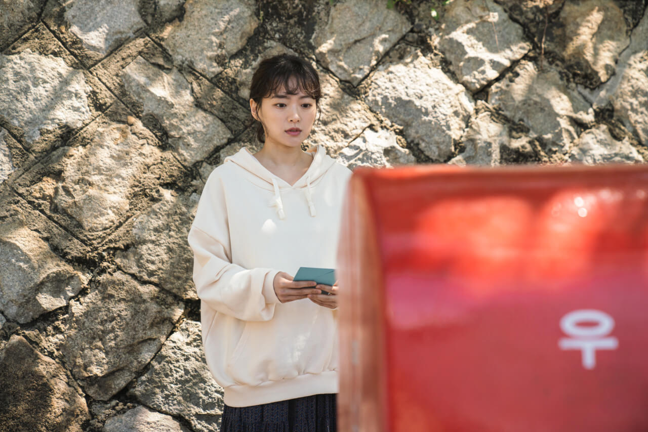 우체통 앞에 서서 편지를 들고 있는 소희