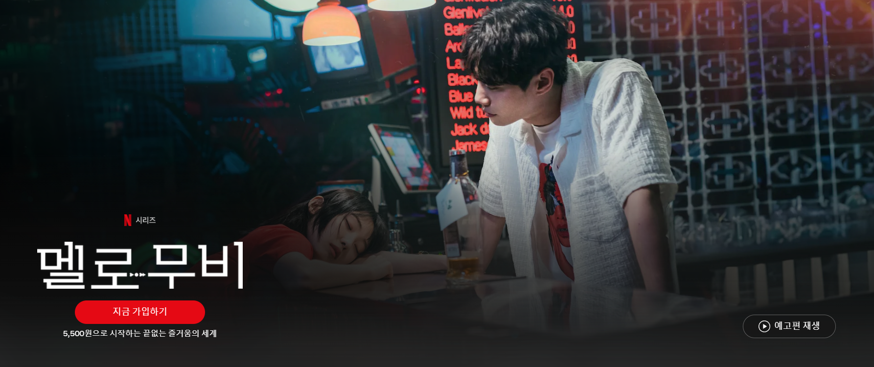 남자가 책상 위에 엎드려 자고 있는 여자를 바라보고 있다.