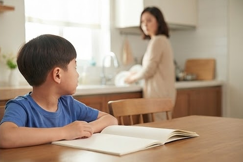 식탁에서 노트를 펴고 엄마 쪽을 살피는 아들