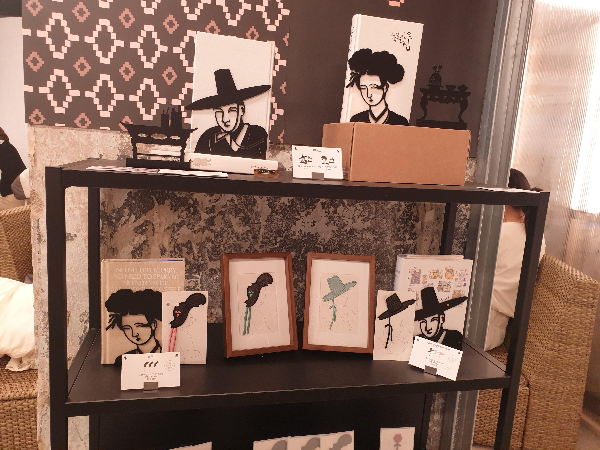 기둥 앞에 검은색 진열장에 갓 모티브의 책갈비 굿즈들이 놓여있다.