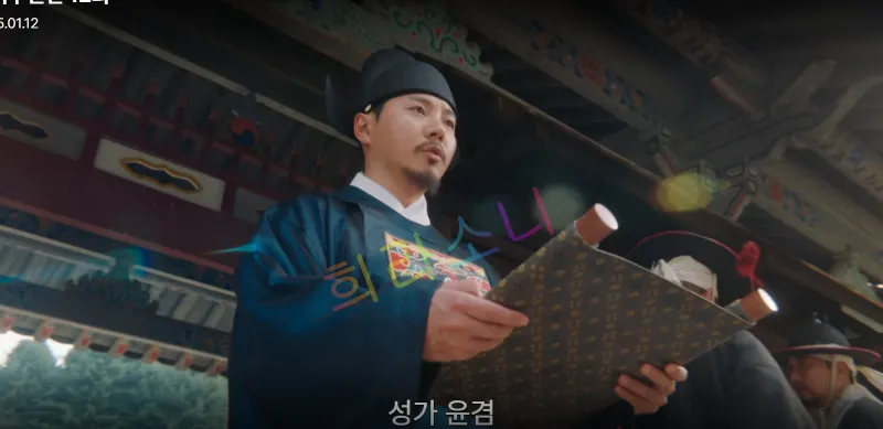 어두운 관리복을 입은 남성이 양산의 문양이 있는 두루마리를 펼쳐 들고 아래를 응시하며 선언하고 있다. 배경에는 전통 건축물의 지붕이 보인다. 자막 