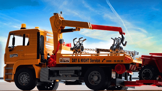 노란색의 트럭형 견인자가 다른 차를 끌고 간다.