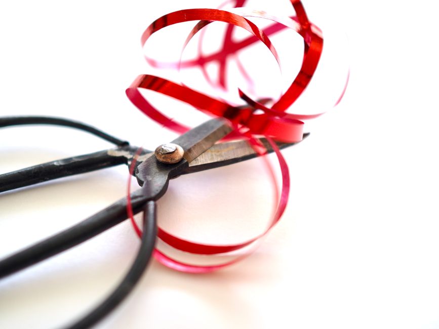 A detailed image of antique scissors with red ribbon on a white surface.