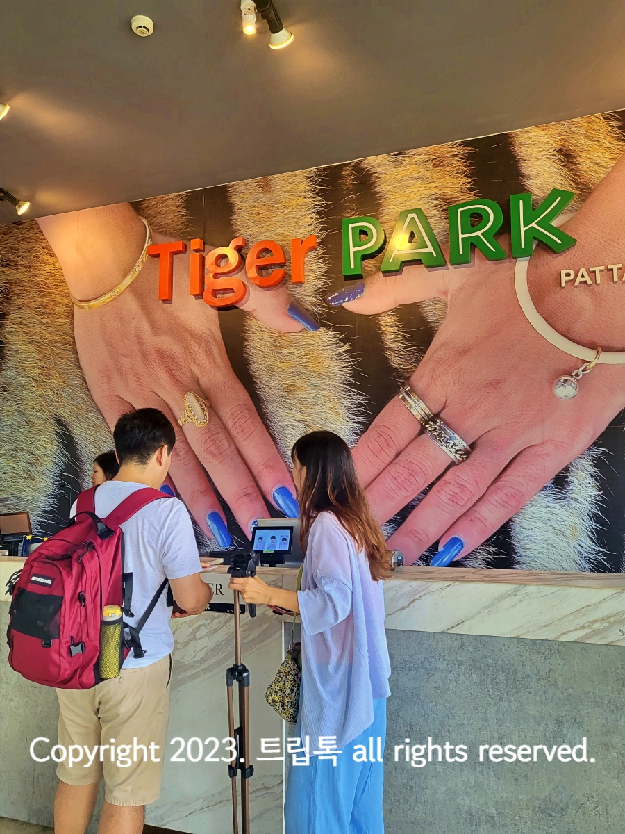 호랑이위로 두손이 올려있는 커다란 사진 앞에서 두사람이 입장권을 사고 있다.